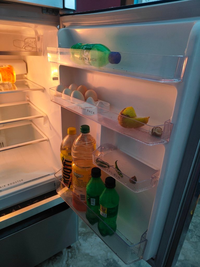 Whirlpool Open triple-door refrigerator interior with deli zone, shelves, egg tray, and drink bottles, highlighting efficient cooling and food freshness