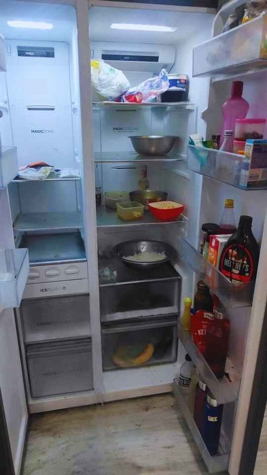 Interior view of a Haier 602L side by side refrigerator showing storage shelves, door racks, and bottom drawers with food containers and bottles