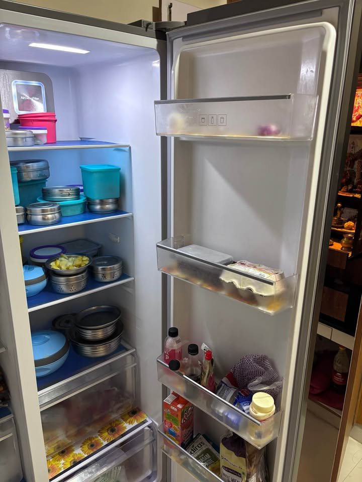 Interior storage view of Voltas Beko 563 L side by side refrigerator showing shelves, door bins, and bottom drawers with food containers.